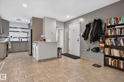 Open-concept living area with tile flooring throughout, featuring a kitchen with stainless steel appliances, light gray cabinetry, and a patterned backsplash - 