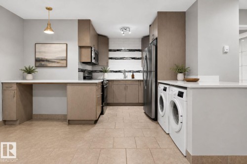 Combined kitchen and laundry area featuring light-toned cabinetry, stainless steel appliances, a tile backsplash, and neutral tile flooring - G14 10148 118 Street Nw, Edmonton, AB 
