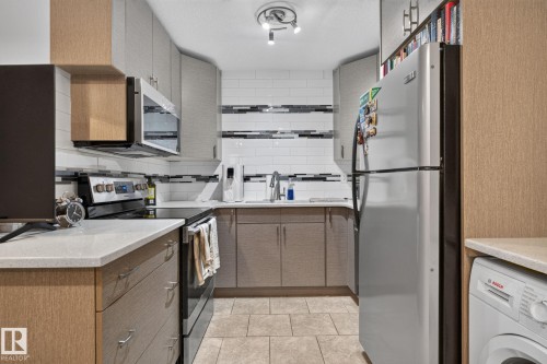 Galley kitchen featuring light wood-finish and gray cabinetry, light countertops, subway tile backsplash, and stainless steel appliances - G14 10148 118 Street Nw, Edmonton, AB 
