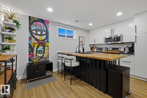 Contemporary basement suite kitchen featuring an expansive island with room for seating, butcher block countertop, black finishes/faucet and stainless steel appliances - 10328 73 Street, Edmonton, AB 