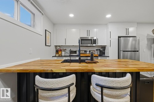Contemporary basement suite kitchen featuring an expansive island with room for seating, butcher block countertop, black finishes/faucet and stainless steel appliances - 10328 73 Street, Edmonton, AB 