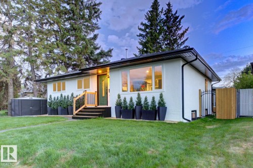 White stucco exterior with black trim, presenting a prominent, modern front entrance with a dark green door and low maintenance landscaping - 10328 73 Street, Edmonton, AB 