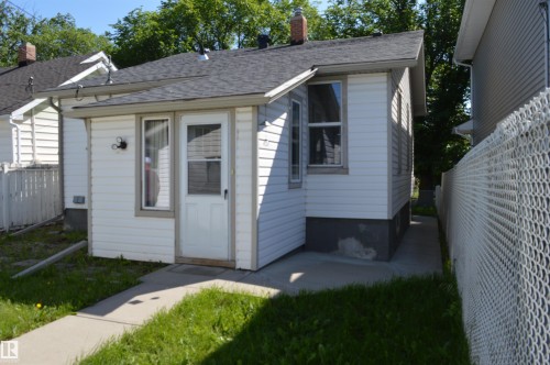 White siding exterior with an attached entryway featuring a glass-paneled door, a single-pane window, and an exterior wall sconce - 11920 78 Street, Edmonton, AB 