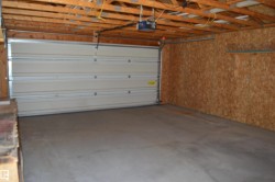Spacious garage featuring a concrete floor, exposed wood ceiling joists, and oriented strand board wall finishes - 