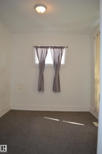 Room featuring a flush mount ceiling light, a window with existing curtain rods, and dark gray carpeting - 11920 78 Street, Edmonton, AB 