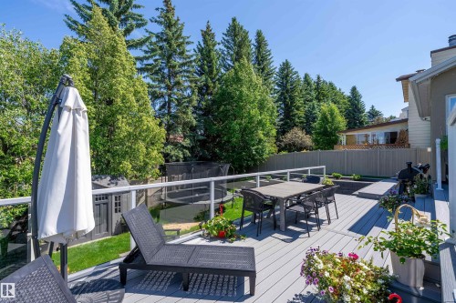 Spacious grey composite decking featuring glass panel railings, built-in planters, and mature tree landscaping - 4 Wentworth Crescent, St. Albert, AB 