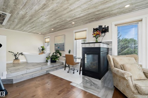 Freestanding soaking tub on a raised platform with tile flooring, featuring a dual-sided fireplace with a tiled surround - 4 Wentworth Crescent, St. Albert, AB 