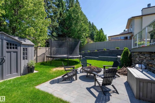 Paver patio with a circular fire pit, surrounded by lush green lawn and mature trees - 4 Wentworth Crescent, St. Albert, AB 