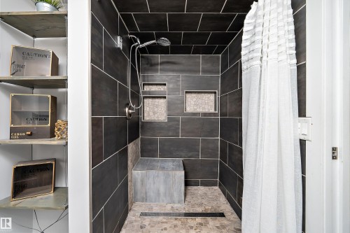 Shower stall featuring dark tile walls, an integrated shower bench, two recessed wall niches with mosaic tile backing, and a handheld showerhead - 4 Wentworth Crescent, St. Albert, AB 