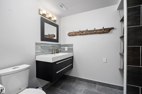Contemporary bathroom featuring a floating black vanity with integrated white sink, a horizontal glass tile backsplash, and a framed mirror - 4 Wentworth Crescent, St. Albert, AB 