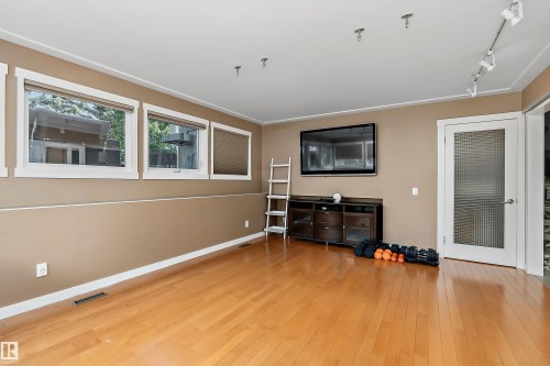Spacious room featuring wood-finish flooring, multiple windows with white trim, and a built-in wall-mounted television - 4 Wentworth Crescent, St. Albert, AB 