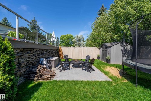Expansive backyard featuring a paver patio with a built-in fire pit, a stacked stone retaining wall, and a raised composite deck with glass panel railing - 4 Wentworth Crescent, St. Albert, AB 