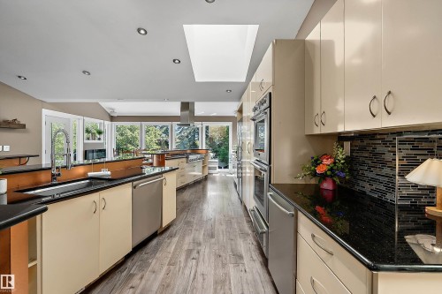 Spacious kitchen featuring extensive cabinetry, dark countertops, wood-finish flooring, stainless steel appliances, and a skylight for natural illumination - 4 Wentworth Crescent, St. Albert, AB 