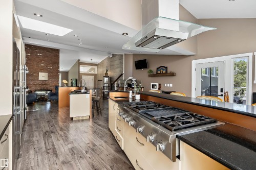 Gourmet kitchen featuring a stainless steel range with griddle, black speckled countertops, an island with sink, cream cabinetry, and wood-finish flooring - 4 Wentworth Crescent, St. Albert, AB 