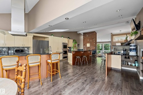 Expansive kitchen and living area featuring wood-finish flooring, a brick accent column, and recessed ceiling lighting - 4 Wentworth Crescent, St. Albert, AB 