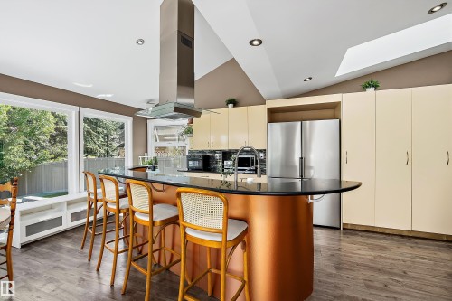 Kitchen featuring a large circular island with a dark countertop and a coppery-toned base, stainless steel appliances, and wood-finish flooring - 4 Wentworth Crescent, St. Albert, AB 