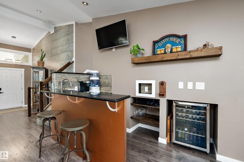 Integrated wet bar with black countertop, stainless steel sink, and built-in beverage refrigerator - 4 Wentworth Crescent, St. Albert, AB 