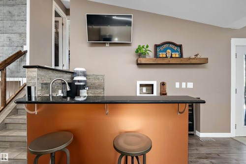 Integrated wet bar featuring a black countertop, stainless steel sink, and wood-finish flooring - 4 Wentworth Crescent, St. Albert, AB 