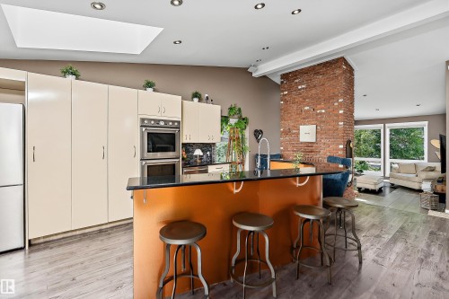 Kitchen featuring an island with a dark countertop, white cabinetry, stainless steel double wall ovens, and wood-finish flooring - 4 Wentworth Crescent, St. Albert, AB 