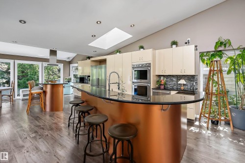 Spacious kitchen featuring a curved island with seating, dark countertops, light cabinetry, and stainless steel appliances - 4 Wentworth Crescent, St. Albert, AB 