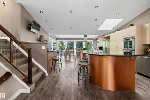 Open concept living space featuring wood-finish flooring, a contemporary kitchen island with a curved copper base and dark countertop, integrated wall ovens, and a skylight - 4 Wentworth Crescent, St. Albert, AB 