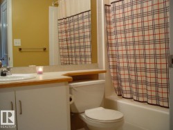 Bathroom featuring a white vanity with integrated sink, a light-toned countertop with wood-finish trim, a recessed mirror, and a white toilet - 