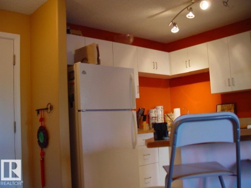 Kitchen area with white cabinetry, track lighting, a full-size refrigerator, and wood-finish countertops - #116 10535 122 St Nw, Edmonton, AB - Indoor Photo Showing Kitchen