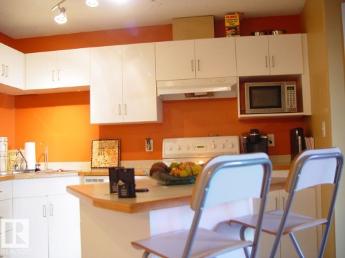 Kitchen featuring white cabinetry, light-toned countertops, a built-in microwave, and track lighting - #116 10535 122 St Nw, Edmonton, AB - Indoor Photo Showing Kitchen