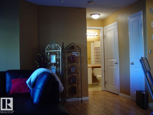Wood-finish flooring throughout, bright white doors, and a bathroom featuring a vanity with a light wood-finish countertop and a wall-mounted light fixture - #116 10535 122 St Nw, Edmonton, AB - Indoor