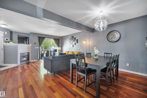 Open-concept living and dining area featuring wood-finish flooring, a corner fireplace with tile surround, and a sliding glass door leading to an outdoor space - #47 2505 42 St Nw, Edmonton, AB 