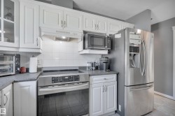 Kitchen featuring white cabinetry, stainless steel appliances, a tile backsplash, and dark speckled countertops - 