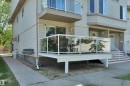 Exterior siding with a ground-level deck featuring glass panel railings, a concrete walkway, and an adjacent entry staircase - #47 2505 42 St Nw, Edmonton, AB 