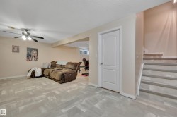 Spacious lower-level living area featuring light-toned flooring, a ceiling fan, painted walls, and a white interior door - 