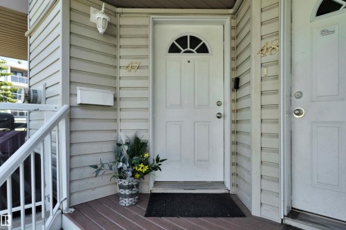 Entryway featuring a white paneled door with an arched transom window, wood-finish decking, and light-colored siding - #47 2505 42 St Nw, Edmonton, AB 