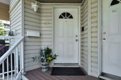 Entryway featuring a white paneled door with an arched transom window, wood-finish decking, and light-colored siding - 