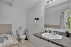Full bathroom featuring a built-in tub with neutral-toned tile surround, a white toilet, and a vanity with a speckled countertop and integrated sink - 