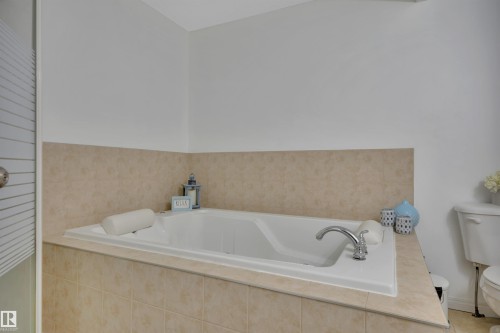 Built-in soaking tub with chrome fixtures, surrounded by neutral-toned tiled walls and a coordinating tiled deck - #47 2505 42 St Nw, Edmonton, AB 