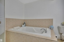 Built-in soaking tub with chrome fixtures, surrounded by neutral-toned tiled walls and a coordinating tiled deck - 