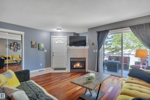 Living area featuring wood-finish flooring, a tiled fireplace, and sliding glass doors opening to an outdoor patio - #47 2505 42 St Nw, Edmonton, AB 