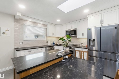 Contemporary kitchen featuring a large central island with a dark stone countertop, white shaker-style cabinetry, and stainless steel appliances - 31 Gariepy Crescent, Edmonton, AB 