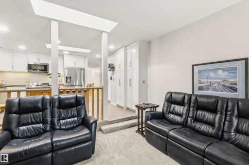 Carpeted living area featuring a vaulted ceiling and a partial wall separating it from a kitchen with stainless steel appliances, a tile backsplash, and light-toned cabinetry - 31 Gariepy Crescent, Edmonton, AB 