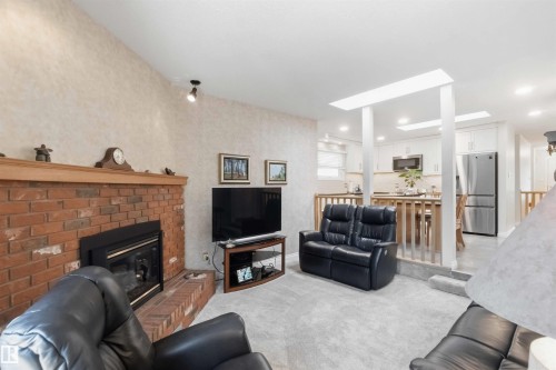Living area featuring a brick fireplace with a wood mantle, vaulted ceiling, and recessed lighting - 31 Gariepy Crescent, Edmonton, AB 