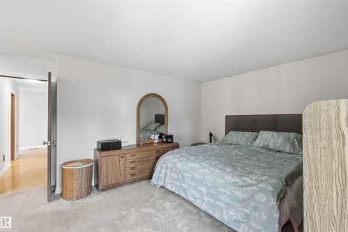 Carpeted bedroom with neutral wall tones and a wood-finish door leading to a hallway with wood-finish flooring - 31 Gariepy Crescent, Edmonton, AB 