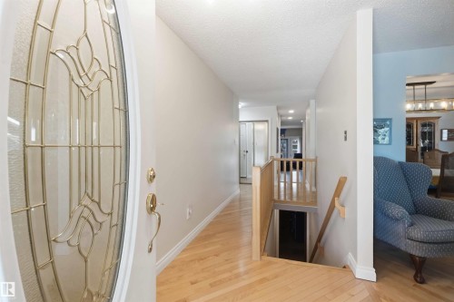 Entryway featuring a decorative glass door with brass hardware, light wood-finish flooring, and a wooden handrail leading to a lower level - 31 Gariepy Crescent, Edmonton, AB 