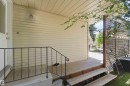 Exterior entrance featuring a wood-finish porch, black metal railing, cream-colored siding, and a lattice privacy screen - 31 Gariepy Crescent, Edmonton, AB 