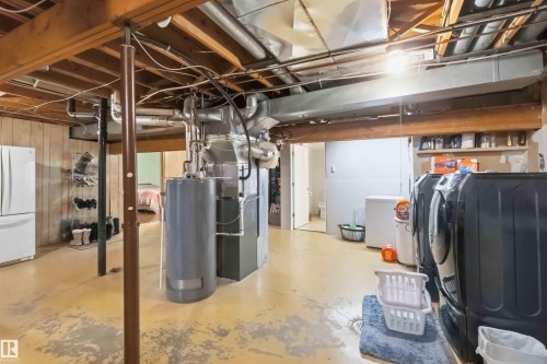 Utility room with exposed ceiling joists and ductwork, featuring a water heater, furnace, and laundry appliances - 31 Gariepy Crescent, Edmonton, AB 