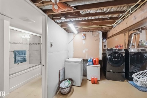 Laundry area featuring exposed ceiling joists and unfinished walls, with a partial view of a finished bathroom - 31 Gariepy Crescent, Edmonton, AB 