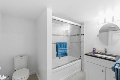 Bathroom featuring a white vanity with dark countertop, round mirror, and a shower-tub combination with sliding glass doors - 31 Gariepy Crescent, Edmonton, AB 