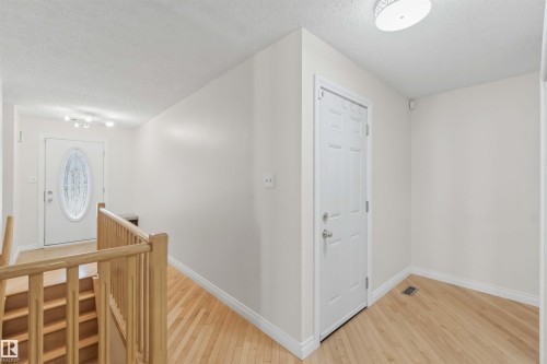 Wood-finish flooring throughout, featuring a white paneled door with hardware, a white door with an oval glass insert, and a light wood staircase with railing - 31 Gariepy Crescent, Edmonton, AB 