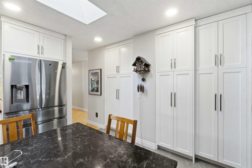 Kitchen featuring extensive white shaker-style cabinetry, stainless steel refrigerator, dark stone-finish countertop, recessed lighting, and a ceiling skylight - 31 Gariepy Crescent, Edmonton, AB 